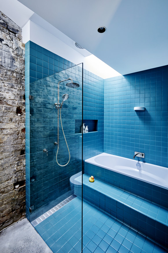 Une porte de la cuisine mène à une salle de bains familiale.  Une partie du mur d'origine de l'écurie est exposée, offrant un contraste de texture avec les carreaux brillants.