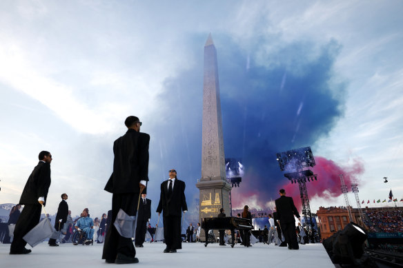 Des artistes en costumes noirs, représentant la société traditionnelle, se produisent lors de la cérémonie d'ouverture des Jeux paralympiques de 2024 tandis que les couleurs du drapeau français explosent dans le ciel parisien.
