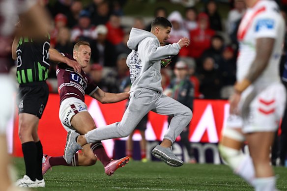 Daly Cherry-Evans tente d'arrêter un envahisseur de pitch lors de l'affrontement avec les Dragons samedi.