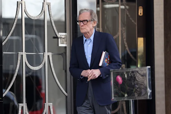 Nighy devant l'hôtel Claridge's à Londres, un livre sous le bras.
