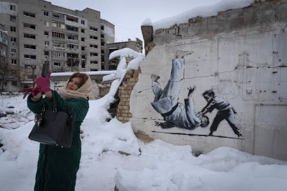 Une femme prend un selfie devant une œuvre d'art réalisée par l'artiste de rue britannique Banksy sur un bâtiment détruit par l'armée russe à Borodyanka, dans la région de Kiev, en Ukraine, en 2022. 