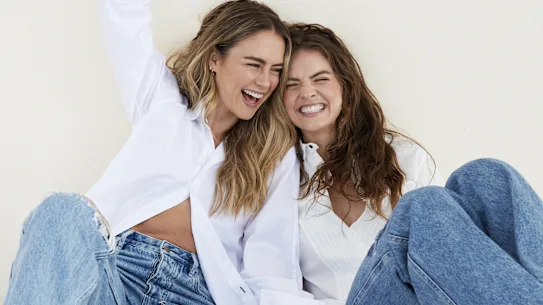 Steph porte un jean et une chemise Bassike. Laura porte une chemise Bassike, un jean Maje.