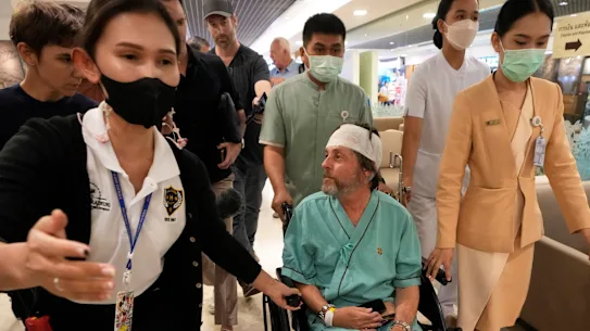 Keith Davis (au centre) est emmené et empêché de parler aux journalistes à l'hôpital Samitivej Srinakarin de Bangkok, en Thaïlande.