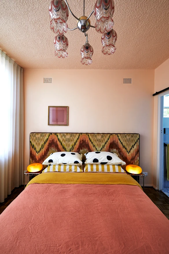 La chambre de couleur pêche comprend une tête de lit et un tapis conçus par Ross. Le plafonnier est un luminaire original d'Etsy, les lampes de chevet proviennent d'IKEA.
