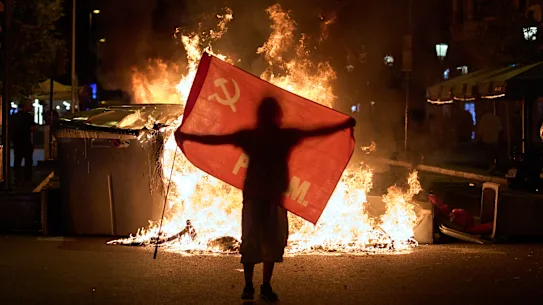 Un manifestant tient un drapeau à côté de poubelles en feu lors d'affrontements avec la police à la suite d'une manifestation contre la crise du logement en Espagne.